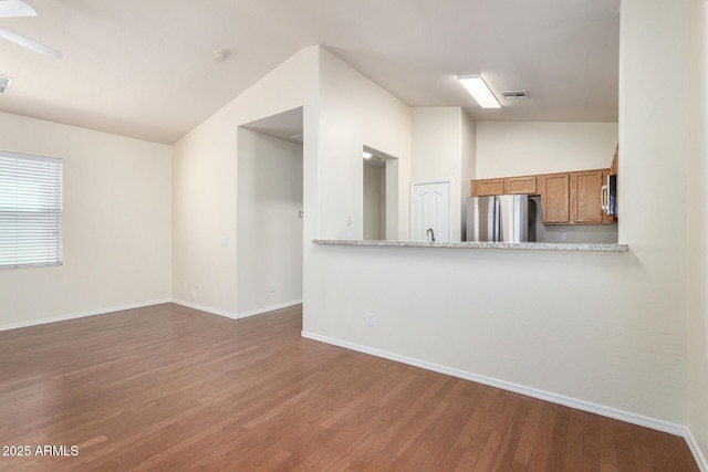 kitchen with wood finished floors, brown cabinetry, visible vents, lofted ceiling, and stainless steel appliances