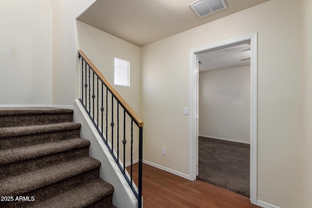 staircase with wood finished floors, visible vents, and baseboards