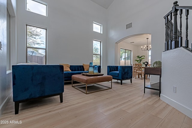 living room with an inviting chandelier, a towering ceiling, and light hardwood / wood-style flooring