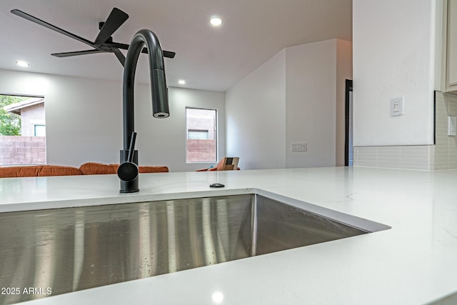 room details with ceiling fan, kitchen peninsula, light stone countertops, and sink