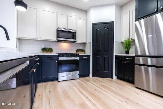 kitchen featuring light hardwood / wood-style floors, appliances with stainless steel finishes, blue cabinetry, backsplash, and white cabinets