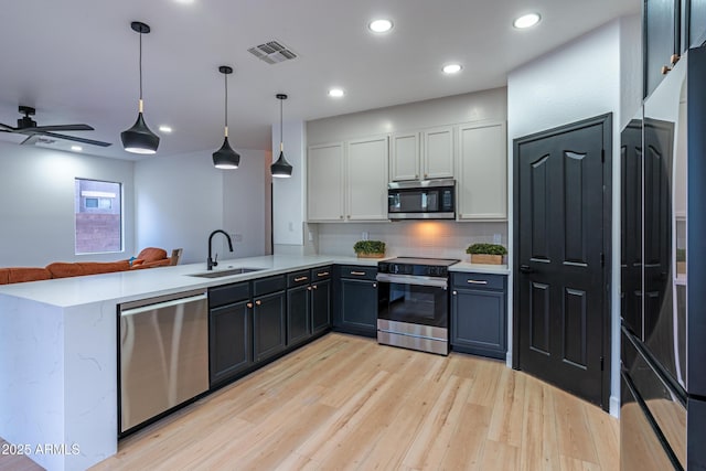 kitchen featuring kitchen peninsula, sink, hanging light fixtures, appliances with stainless steel finishes, and white cabinets