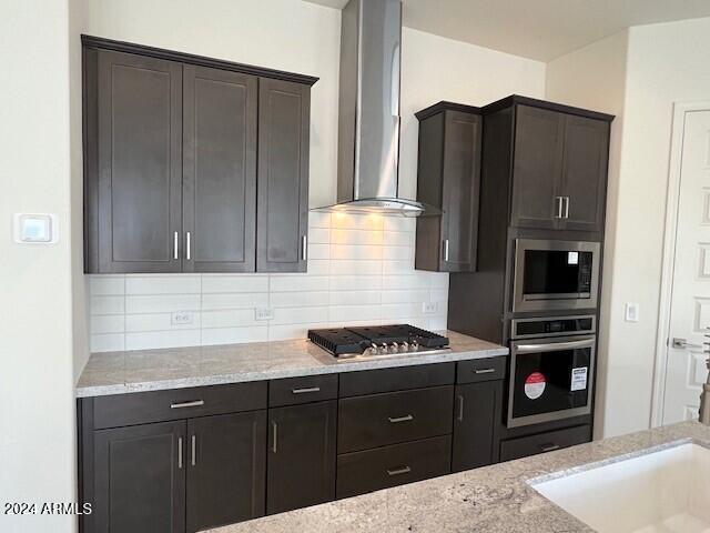 kitchen with tasteful backsplash, light stone countertops, wall chimney exhaust hood, and appliances with stainless steel finishes