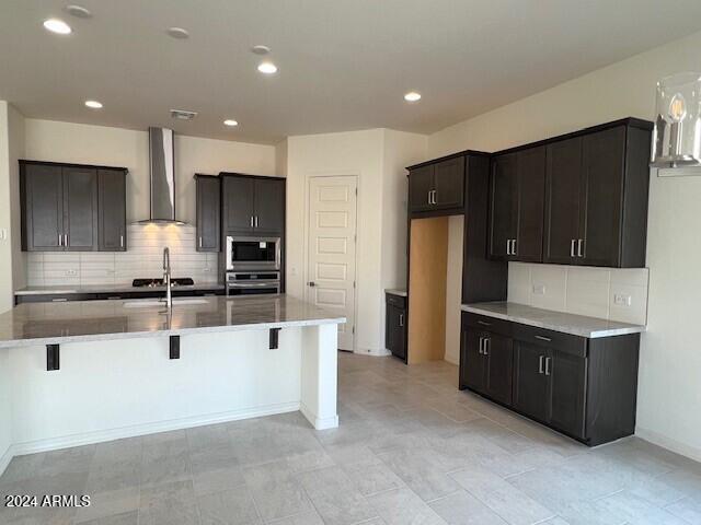 kitchen featuring appliances with stainless steel finishes, a breakfast bar, an island with sink, sink, and wall chimney range hood