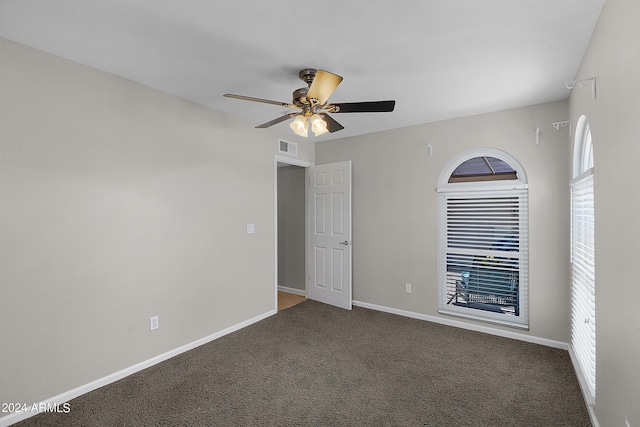 empty room featuring a ceiling fan, visible vents, dark carpet, and baseboards