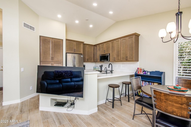 6831 S Coral Gable Dr, Chandler, AZ 85249 - kitchen featuring appliances with stainless steel finishes, vaulted ceiling, backsplash, a kitchen bar, and light wood-style flooring