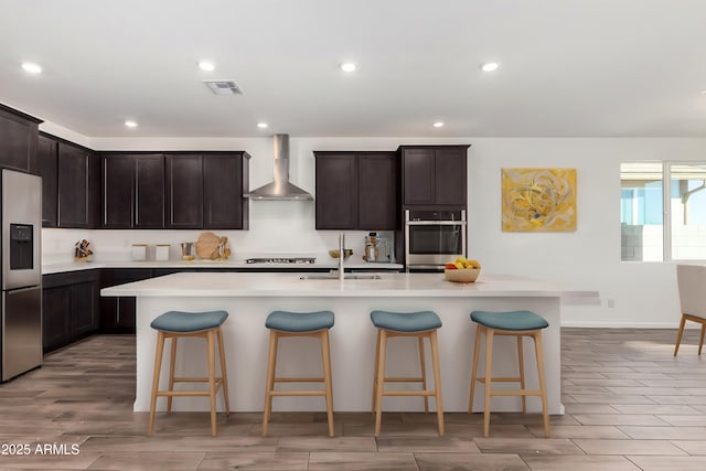 kitchen featuring wall chimney exhaust hood, sink, a breakfast bar area, an island with sink, and stainless steel appliances