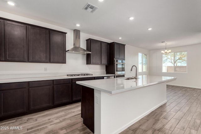 kitchen featuring pendant lighting, sink, a kitchen island with sink, dark brown cabinets, and wall chimney exhaust hood