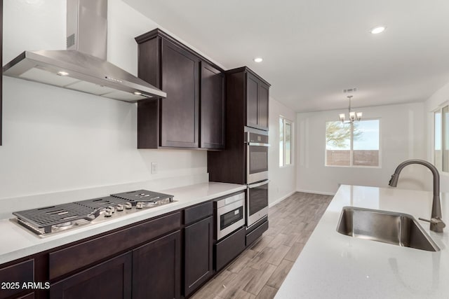 kitchen featuring wall chimney exhaust hood, sink, decorative light fixtures, light hardwood / wood-style flooring, and appliances with stainless steel finishes