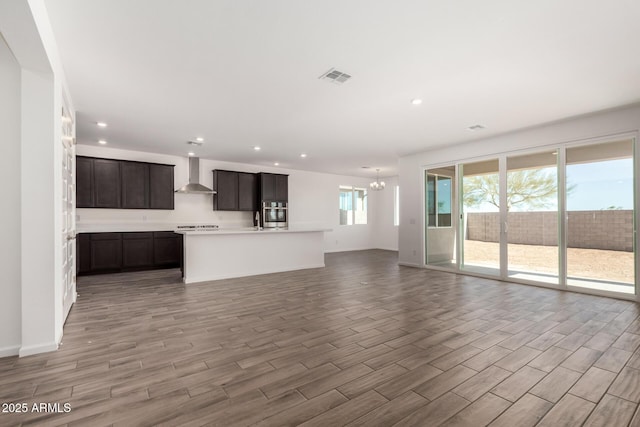 kitchen featuring a notable chandelier, light countertops, open floor plan, a kitchen island with sink, and wall chimney exhaust hood