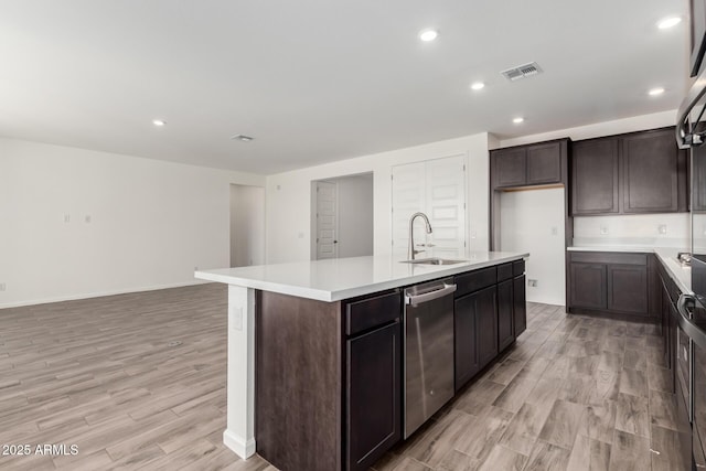 kitchen with dishwasher, an island with sink, sink, dark brown cabinets, and light hardwood / wood-style flooring