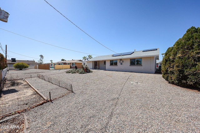 rear view of house featuring roof mounted solar panels and fence