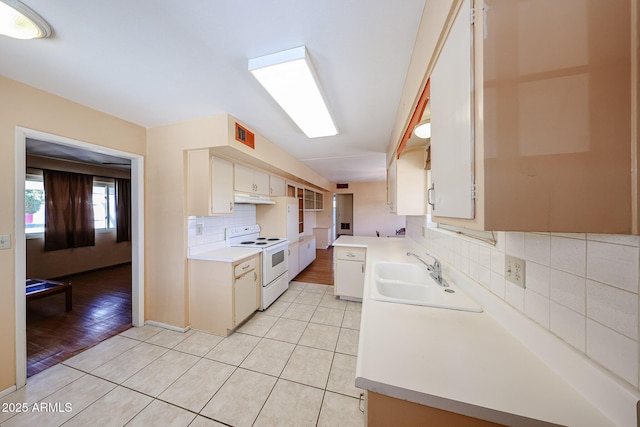 kitchen with under cabinet range hood, light countertops, light tile patterned floors, white range with electric stovetop, and a sink