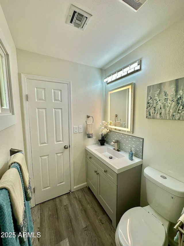 bathroom with toilet, hardwood / wood-style floors, vanity, and decorative backsplash