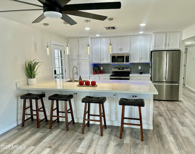 kitchen with pendant lighting, stainless steel appliances, a kitchen breakfast bar, and white cabinets