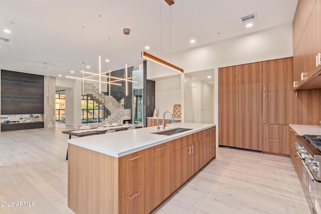 kitchen with hanging light fixtures, light wood-type flooring, an island with sink, ceiling fan with notable chandelier, and sink