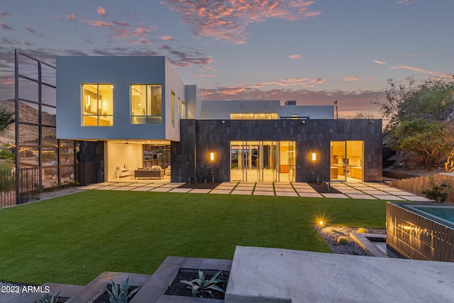 back house at dusk with a fire pit, a balcony, a lawn, and a patio area