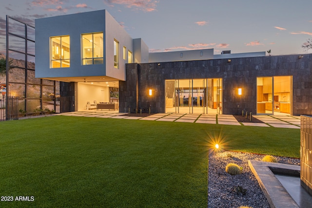 back house at dusk featuring a yard and a patio