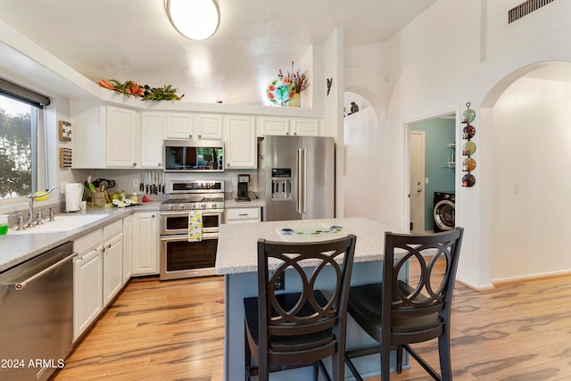 kitchen with high quality appliances, sink, a center island, white cabinetry, and light hardwood / wood-style floors