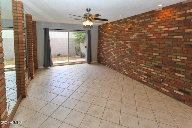 unfurnished room with ceiling fan, brick wall, light tile patterned floors, and a textured ceiling