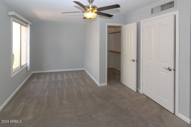 unfurnished bedroom with dark carpet, multiple windows, a spacious closet, and ceiling fan