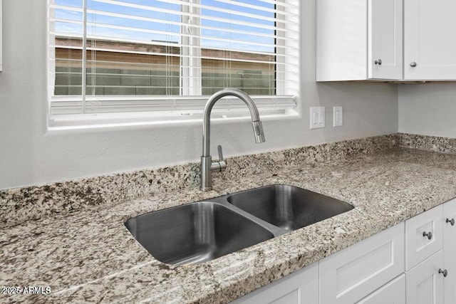 room details featuring light stone countertops, white cabinets, and a sink