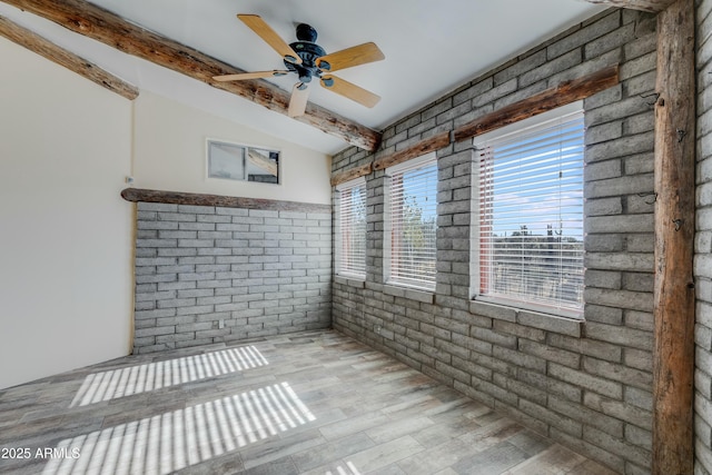 spare room featuring beam ceiling, ceiling fan, light wood-type flooring, and brick wall