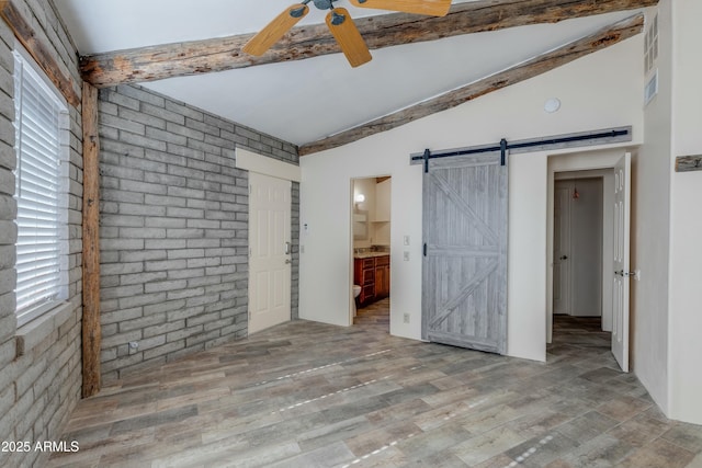 unfurnished bedroom with ensuite bathroom, ceiling fan, light wood-type flooring, a barn door, and lofted ceiling with beams