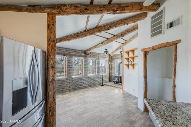 kitchen with lofted ceiling with beams, brick wall, stainless steel fridge, a wood stove, and stone countertops