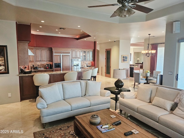 living room featuring a raised ceiling and ceiling fan with notable chandelier