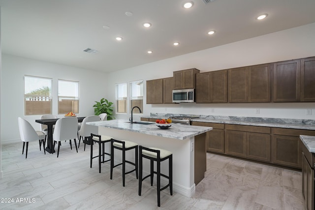 kitchen with a breakfast bar, sink, an island with sink, appliances with stainless steel finishes, and light stone counters