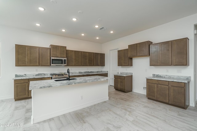 kitchen with a center island with sink, dark brown cabinets, light stone counters, and sink