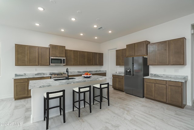 kitchen featuring a breakfast bar, a center island with sink, sink, light stone countertops, and appliances with stainless steel finishes