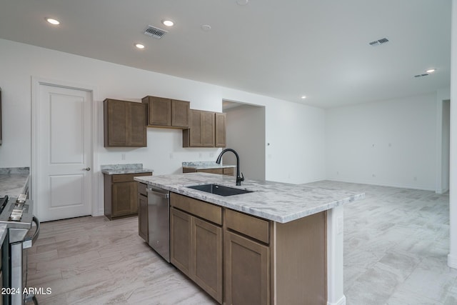 kitchen featuring light stone countertops, an island with sink, stainless steel appliances, and sink