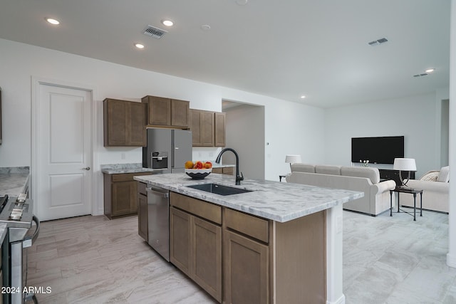 kitchen with a kitchen island with sink, sink, stainless steel appliances, and light stone counters