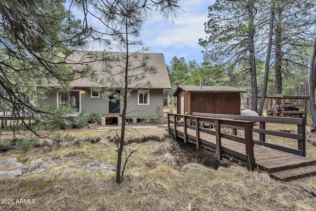 back of property featuring a deck, an outdoor structure, and a shingled roof