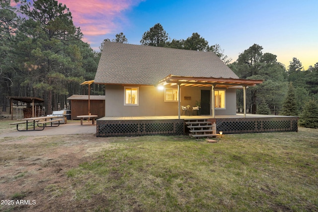 back of property featuring a lawn, stucco siding, a shingled roof, and a wooden deck