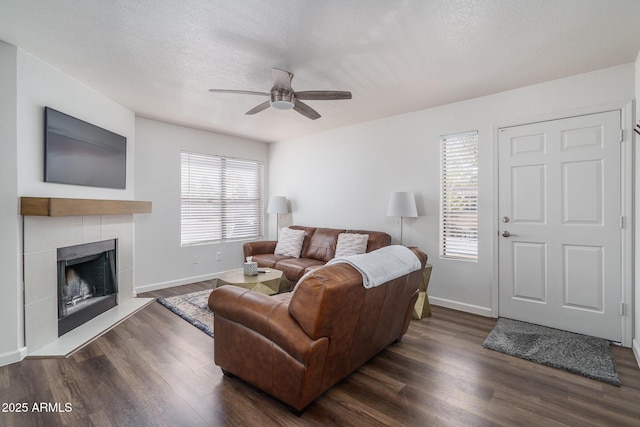 living area featuring wood finished floors, a tiled fireplace, baseboards, and ceiling fan
