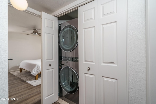clothes washing area featuring wood finished floors, laundry area, a textured ceiling, ceiling fan, and stacked washing maching and dryer