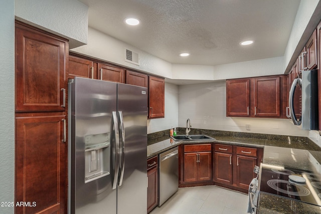 kitchen with visible vents, a sink, dark stone countertops, reddish brown cabinets, and appliances with stainless steel finishes