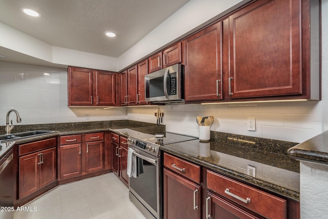 kitchen featuring a sink, reddish brown cabinets, dark stone countertops, and appliances with stainless steel finishes