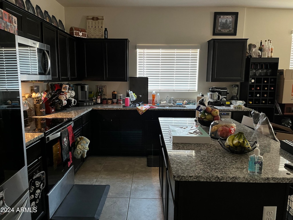 kitchen featuring light stone counters, appliances with stainless steel finishes, light tile patterned floors, and a center island