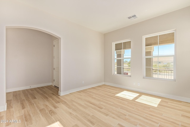 spare room with arched walkways, visible vents, light wood-style flooring, and baseboards