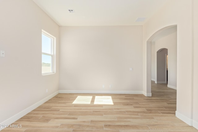 spare room featuring arched walkways, visible vents, light wood-style flooring, and baseboards