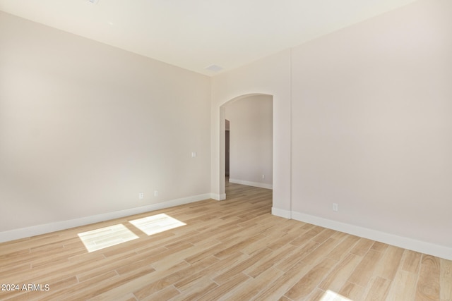 spare room featuring arched walkways, light wood finished floors, and baseboards