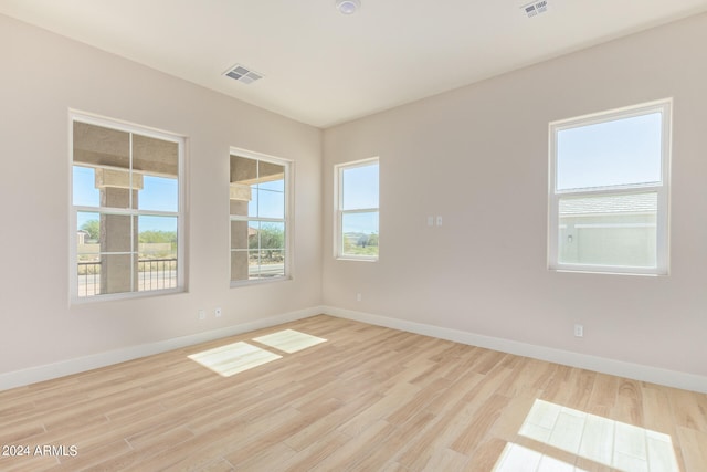 empty room with light wood-style floors, visible vents, and baseboards