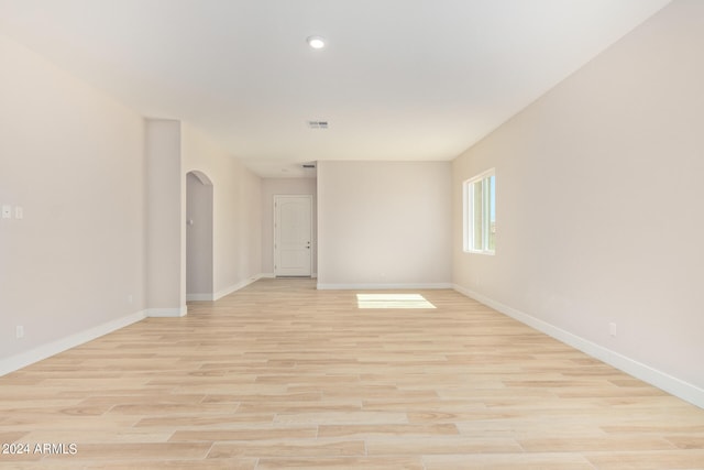 empty room with arched walkways, visible vents, light wood-style flooring, and baseboards