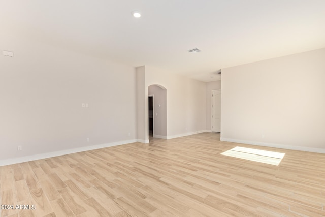 unfurnished room with arched walkways, baseboards, visible vents, and light wood finished floors