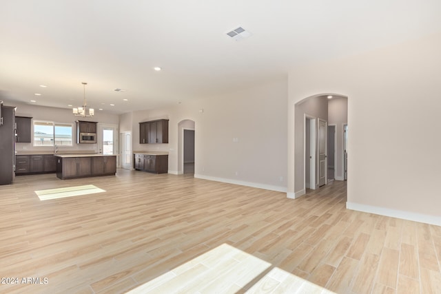 unfurnished living room with arched walkways, visible vents, light wood-style flooring, and baseboards