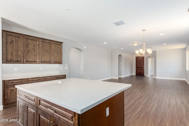 kitchen featuring arched walkways, a kitchen island, open floor plan, light countertops, and dark wood finished floors